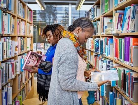 Two women reading books in between book shelves.