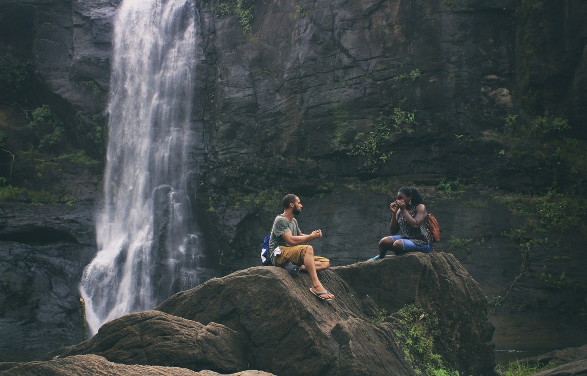 Mies ja nainen istuvat kalliolla. Takana on vesiputous.