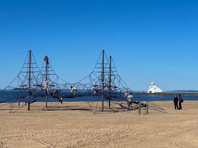 A jungle gym at the beach, a lighthouse in the background.