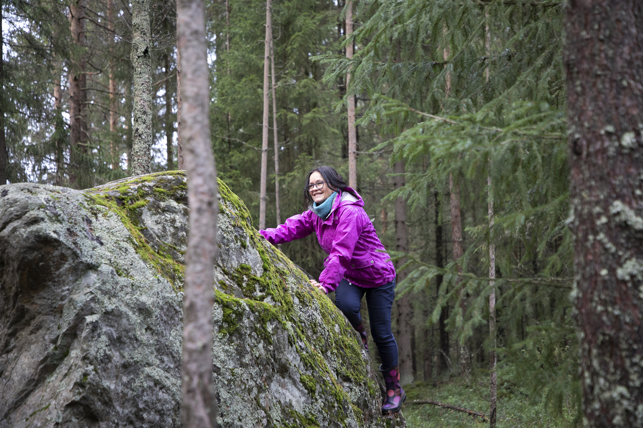 Nainen kiipeää kivelle metsässä.