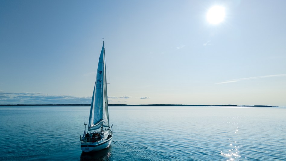 Sinisellä merellä oleva purjevene, joka purjehtii kohti aurinkoa. 