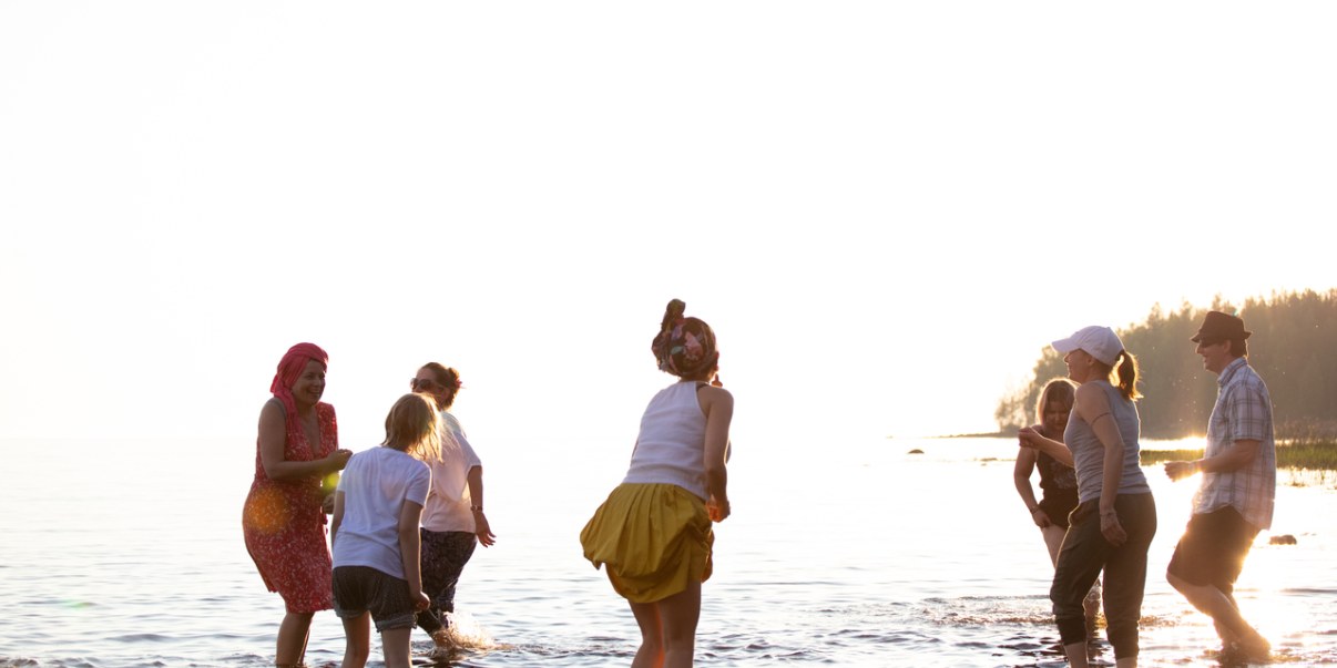 Kesä, ihmisiä kahlaa meressä. Iloinen ja riemukas tunnelma.