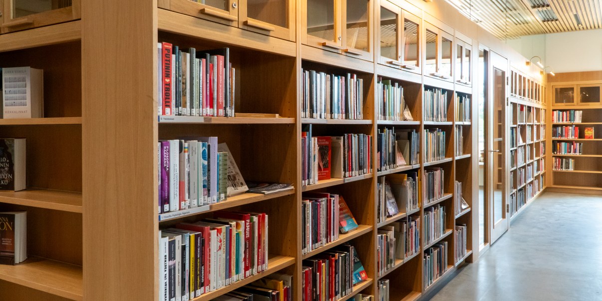 Kirjahyllyjä täynnä kirjoja, avoyläpuolella lasiovellisia hyllyjä. Hyllyjen välissä lasiovi.