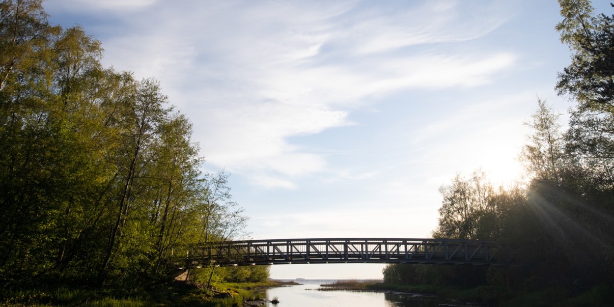 Joen yli menee silta, taustalla meri. Taivaalla valkoisia pilven haituvia.