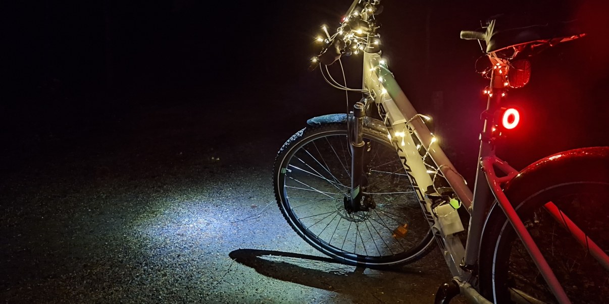 Pyörä pimeässä. Pyörässä paljon valoja, koristevalot tangossa, valkoinen etuvalo ja punainen takavalo.