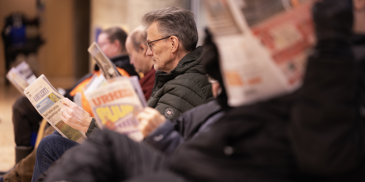 Henkilöitä istumassa vierekkäin ja lukemassa lehtiä.