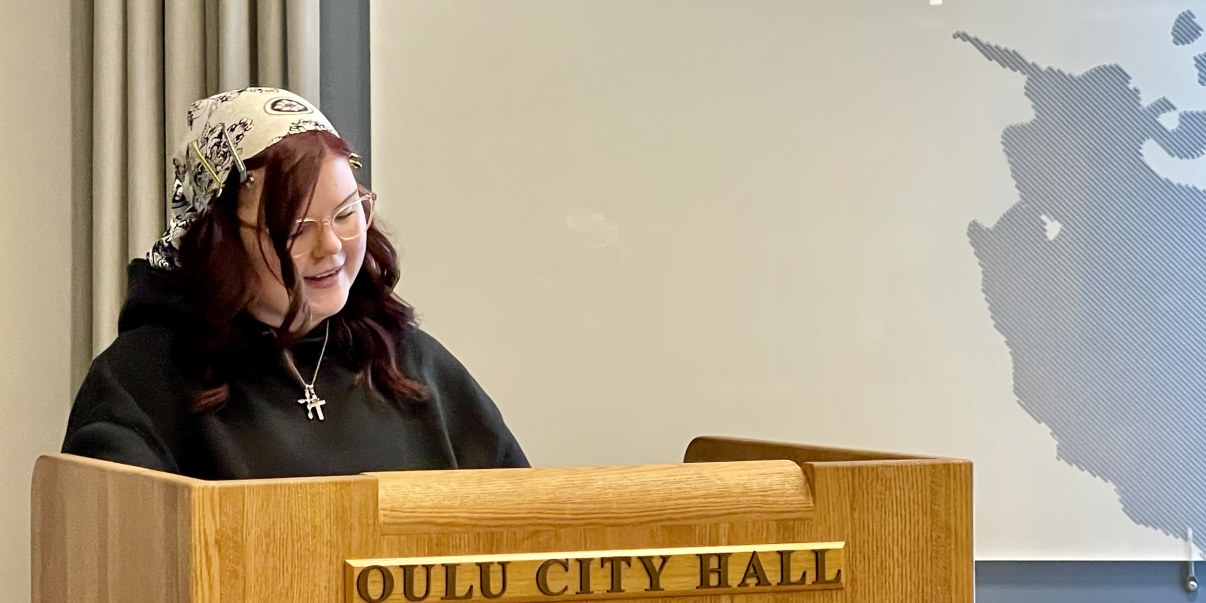 Nuorisovaltuuston puheenjohtaja puhuu kaupunginvaltuuston kokouksessa, kuvassa puheenjohtaja Emma Kanninen puhujapöntön takana. Puhujapöntössä lukee Oulu City Hall.