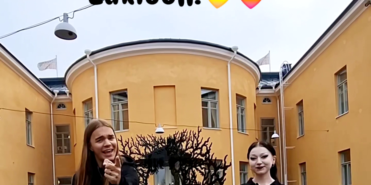 Kaksi opiskelijaa Lyseon lukion pihalla katsomassa kameraan kutsuen hakemaan opiskelijaksi