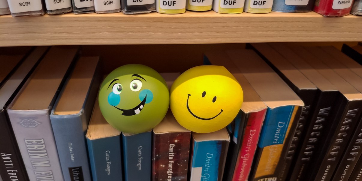 Kaksi pallonmuotoista puristeltavaa esinettä kirjojen päällä.