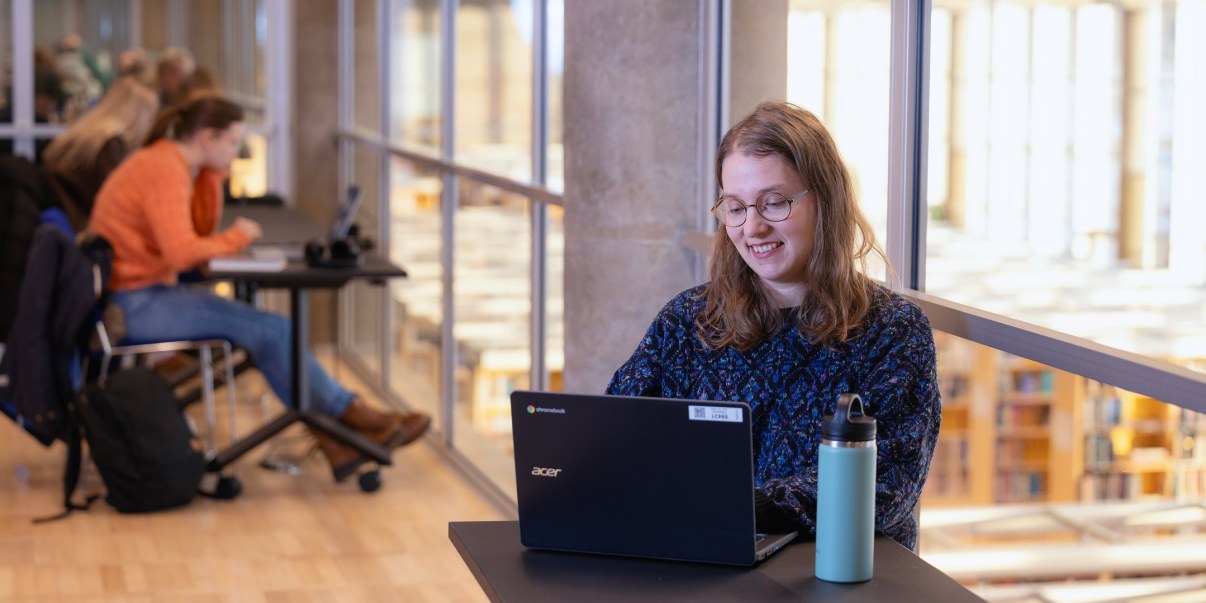 Henkilö työskentelee kannettavalla tietokoneella kirjastossa.