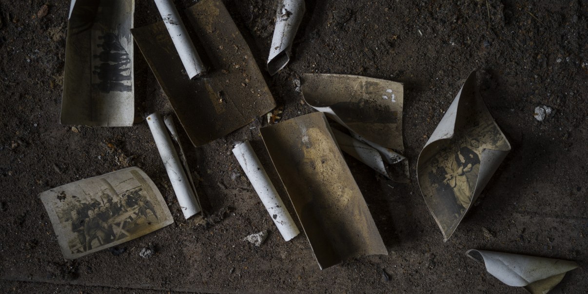 Likaisia, vanhoja, käpristyneitä valokuvia likaisella lattialla.