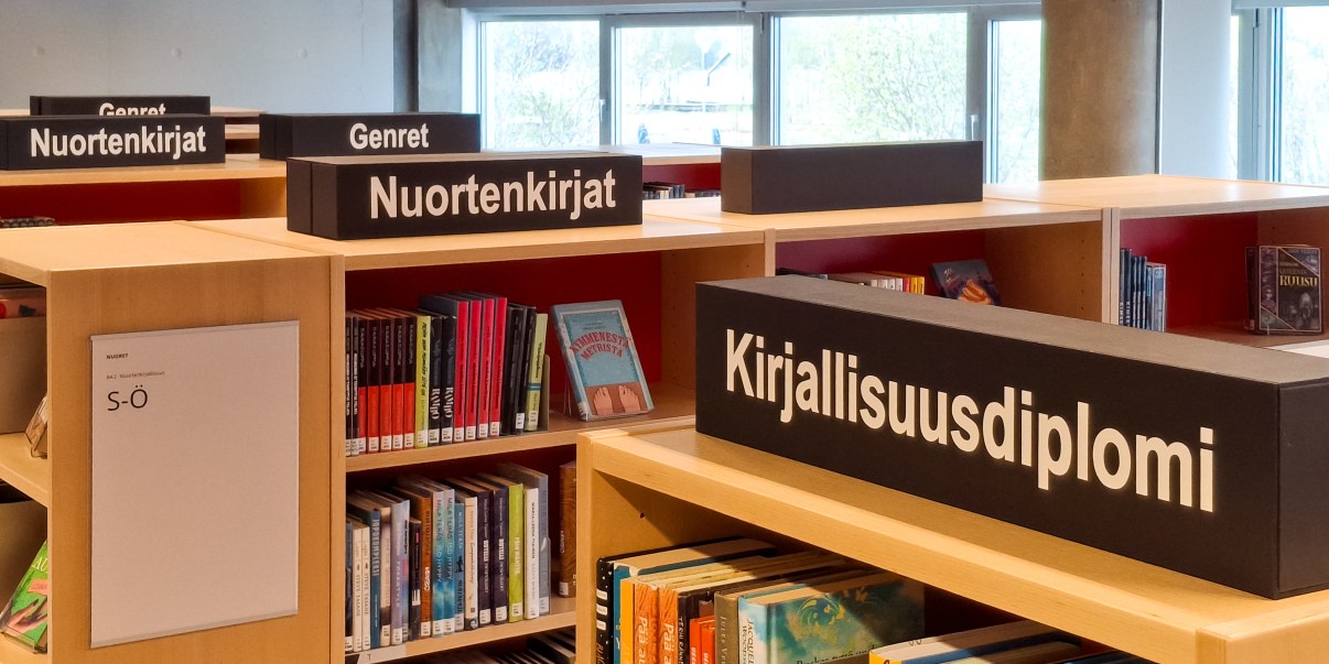 Kirjahyllyjä joiden päällä opastekylttejä.