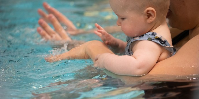 Pieni lapsi vanhempansa sylissä uima-altaassa.