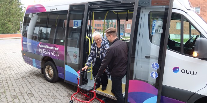 Asiakas laskeutuu Onni-palveluliikenteen bussin kyydistä rollaattorin kanssa kuljettajan avustaessa.