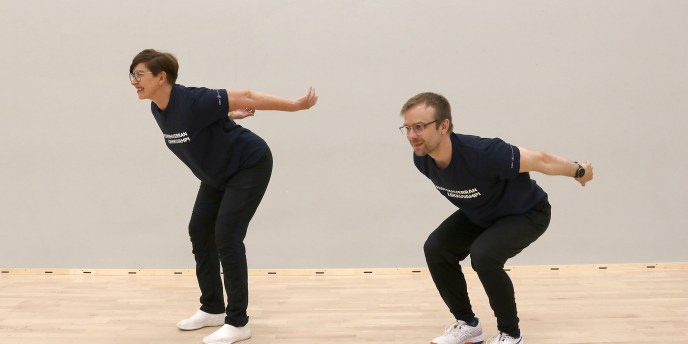 kaksi henkilöä kyykkää mäkihyppääjän asennossa