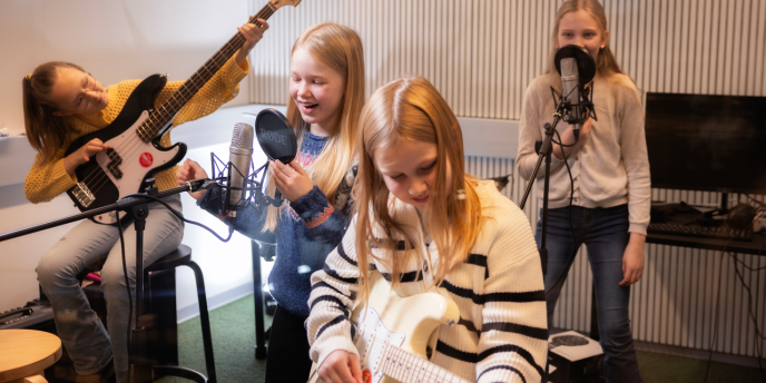 Neljä iloista nuorta soittaa ja laulaa bänditilassa.