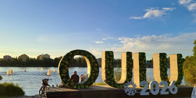 Betoniset isot OULU-kirjaimet suiston rannassa. Ilta-aurinko heijastuu kirjaimiin.