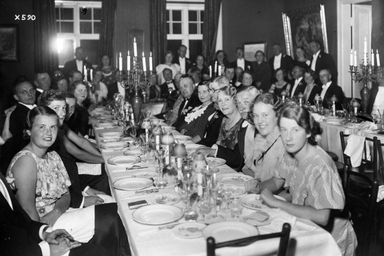 Ihmisiä juhlatunnelmissa katetun ruokapöydän äärellä.