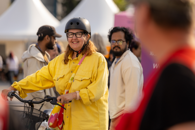Woman in a yellow coat with a helmet walking her bicycle