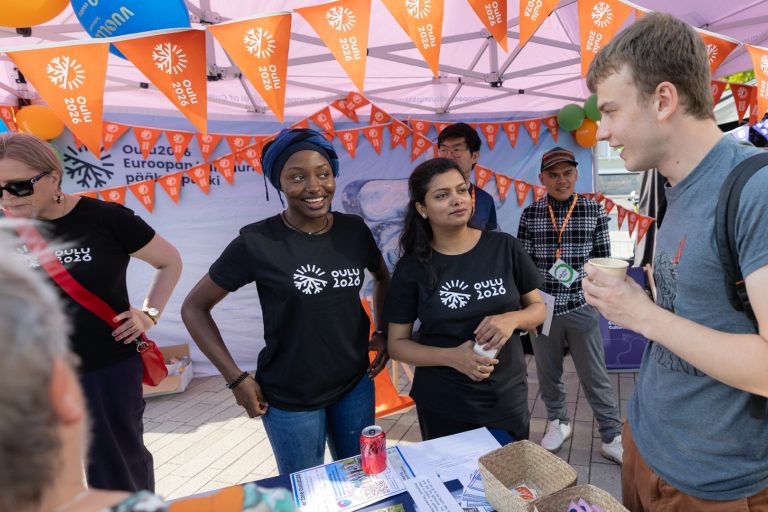 Two women at an exhibition booth, flag garlands in the background