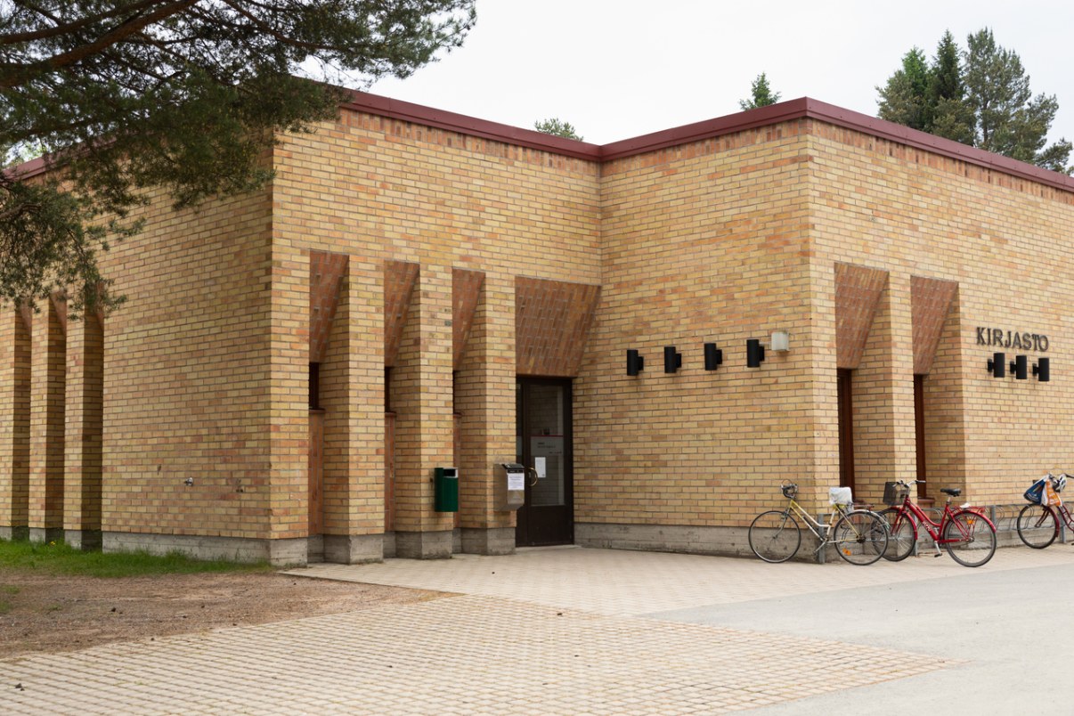 Light brown brick building with recessed windows. The entrance is located in a recess. On the wall, a sign is saying 'library'.