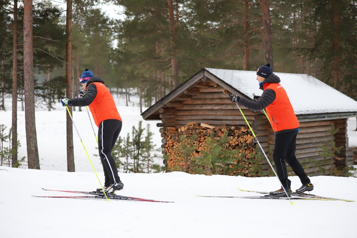 Two people are skiing past a lodge