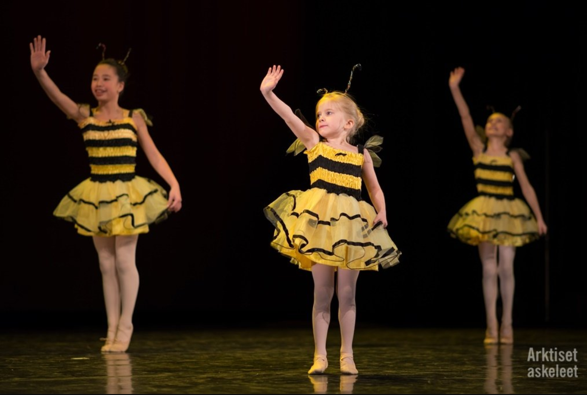 Kolme lasta tanssii lavalla pukeutuneina mehiläisiksi