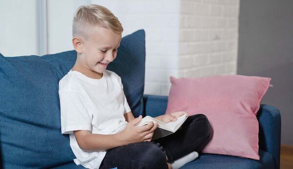 Poika istuu sohvalla lukemassa kirjaa
