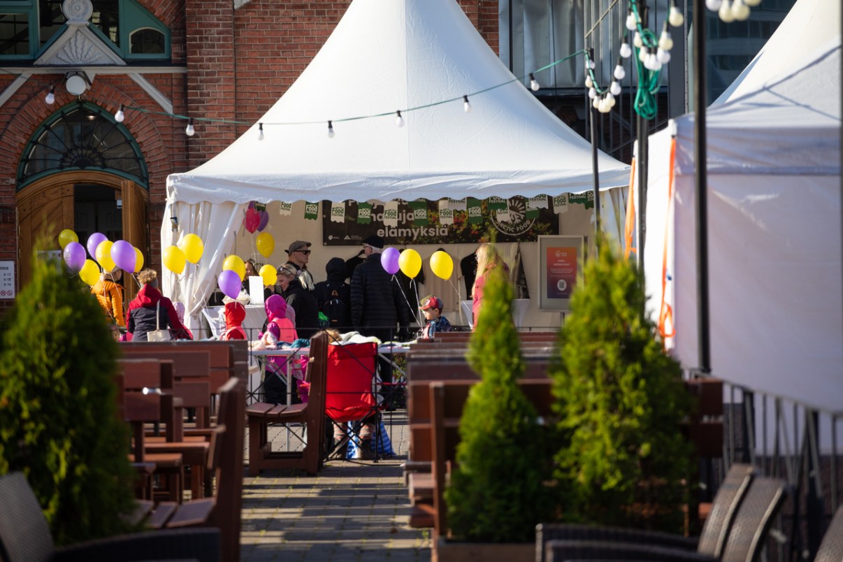 Valkoinen ravintoplateltta, jonka edessä ihmisiä ja ruokailupöytiä.