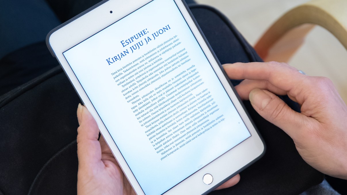 Tabletti henkilön käsissä, ruudulla auki e-kirja.