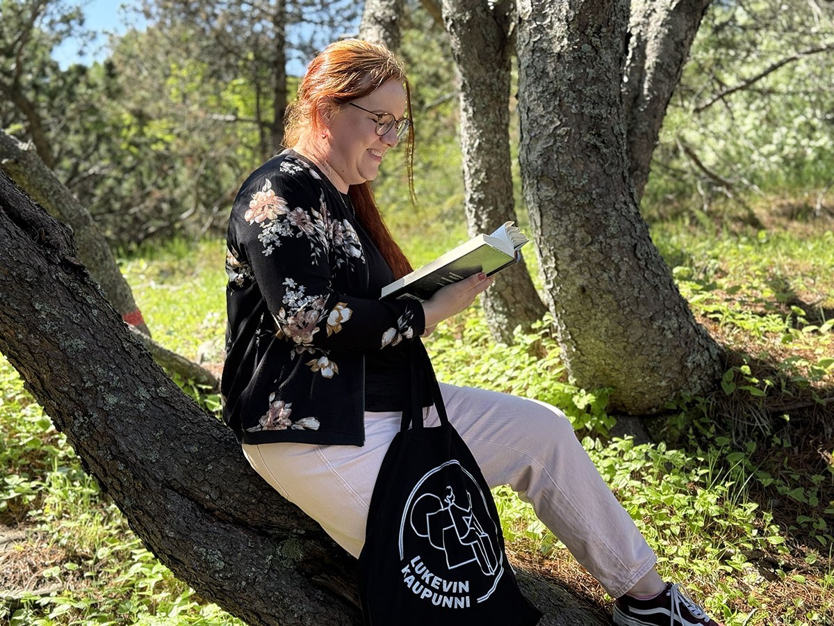 Nainen istuu puun rungolla lukemassa kirjaa