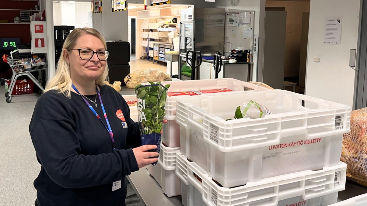 Prikkakeskuksen projektipäällikkö Katja Suhonen seisoo lahjoitettujen ruokien vieressä ja esittelee tuoretta basilikaa.
