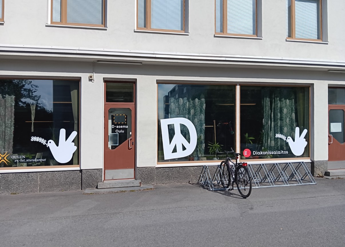 Kerrostalon kivijalkatila jossa isot ikkunat ja ovi, ikkunassa iso D-kirjain.