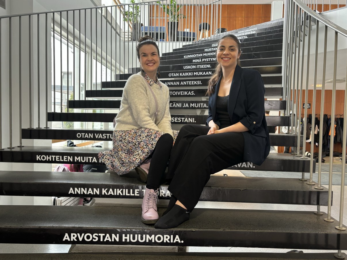 Hymyilevät naiset istuvat koulun portaikossa