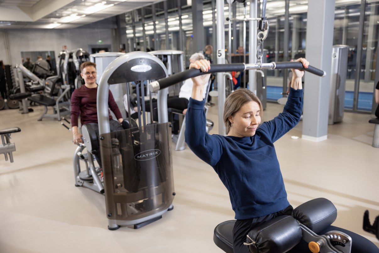 Naiset harjoittelee kuntosalin laitteilla.