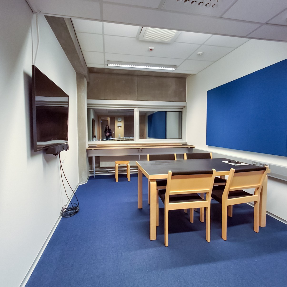 Kokoushuone jossa pöydän ympärillä neljä tuolia, seinällä näyttö.