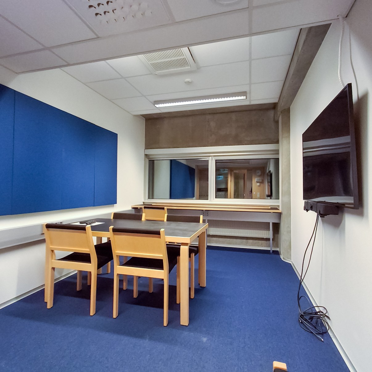 Kokoushuone jossa pöydän ympärillä neljä tuolia, seinällä näyttö.