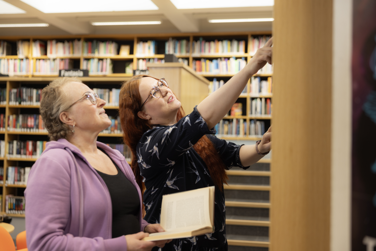 Kirjaston työntekijä esittelee asiakkaalle kirjoja.