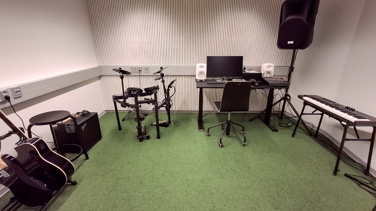 Huone jossa kitaroita, sähkörummut, tietokone ja kosketinsoitin.