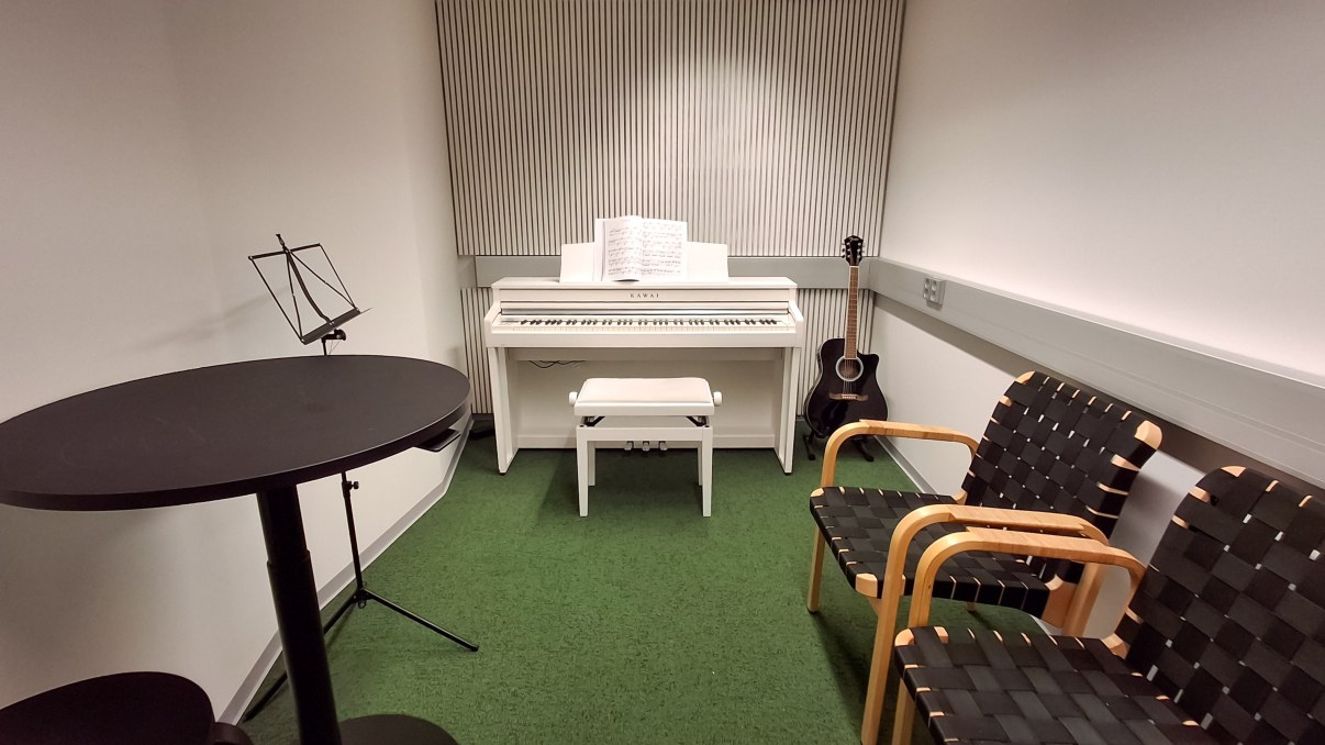 Huone jossa sähköpiano, akustinen kitara, tuoleja ja pieni pöytä.