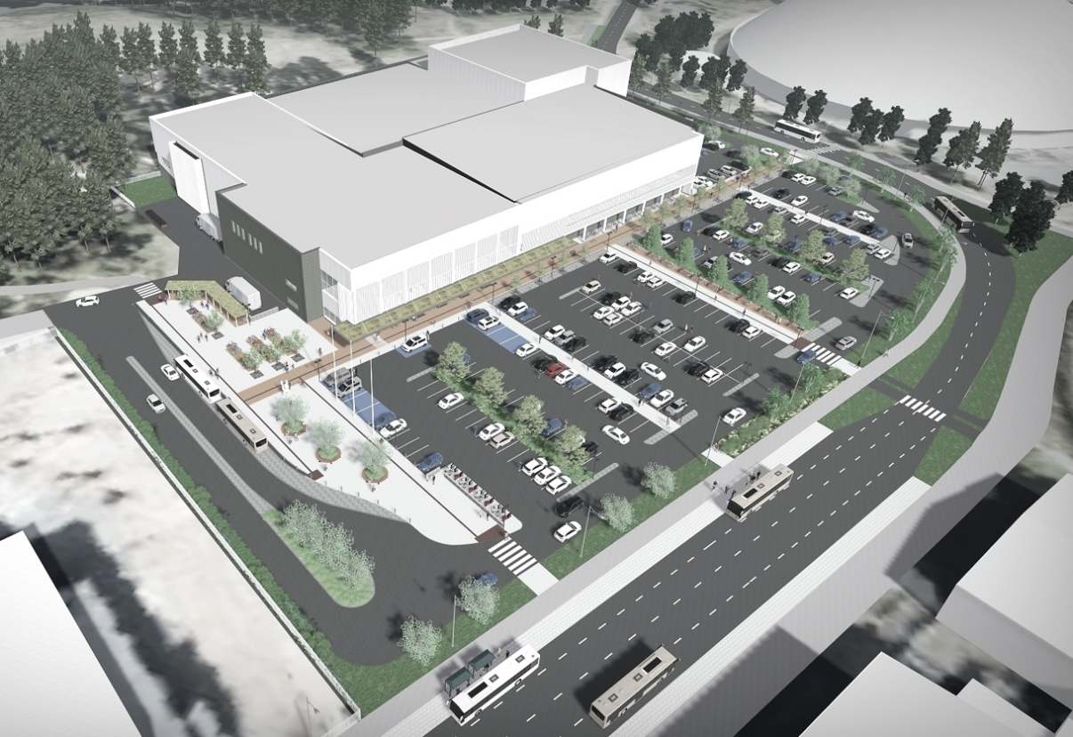 Suuri valkoinen rakennus, jonka edessä pysäköintipaikat. Vieressä kulkee busseja tiellä.