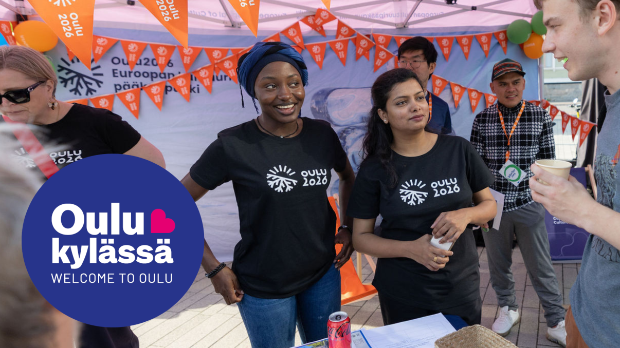 Kaksi ihmistä seisoo esittelypisteellä puhumassa asiakkaalle. Taustalla on oransseja lippuviirejä. Kuvan päällä on Oulu kylässä -festivaalin logo.