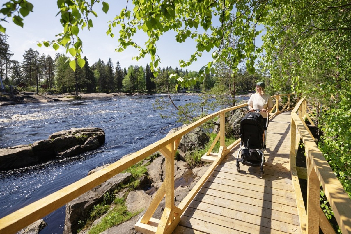 Äiti työntää lastenvaunuja Koitelinkosken rannalla. 