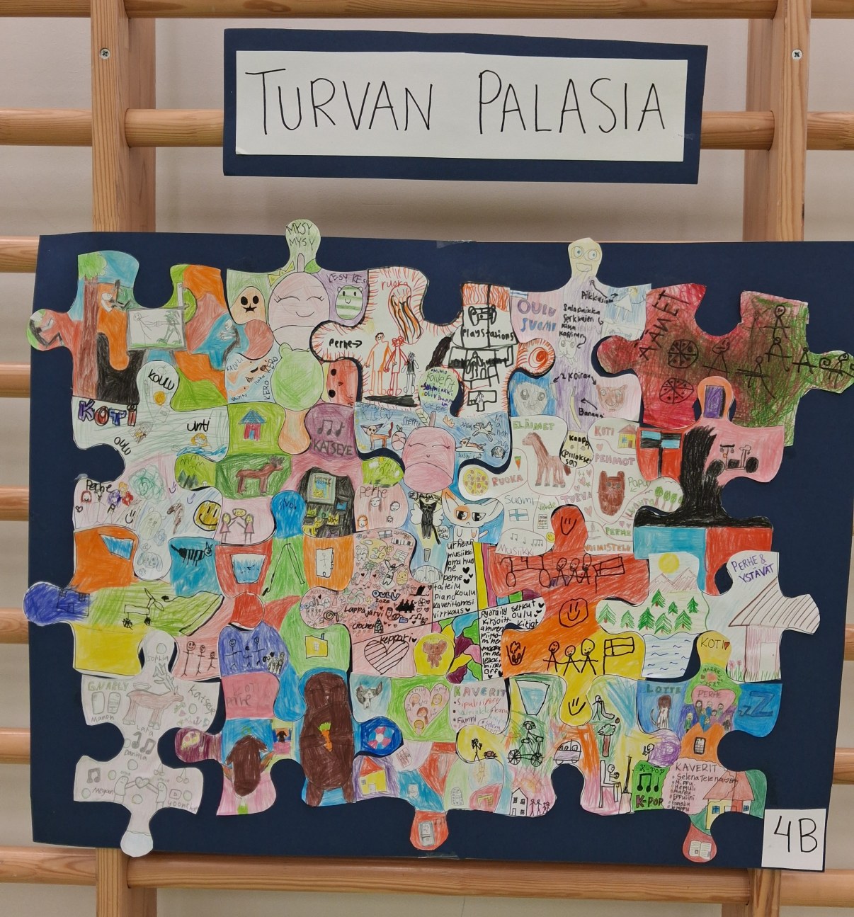 Suuri musta kartonki, jolle on liimattu paljon pieniä palapelin palasten muotoisia taideteoksia.  
