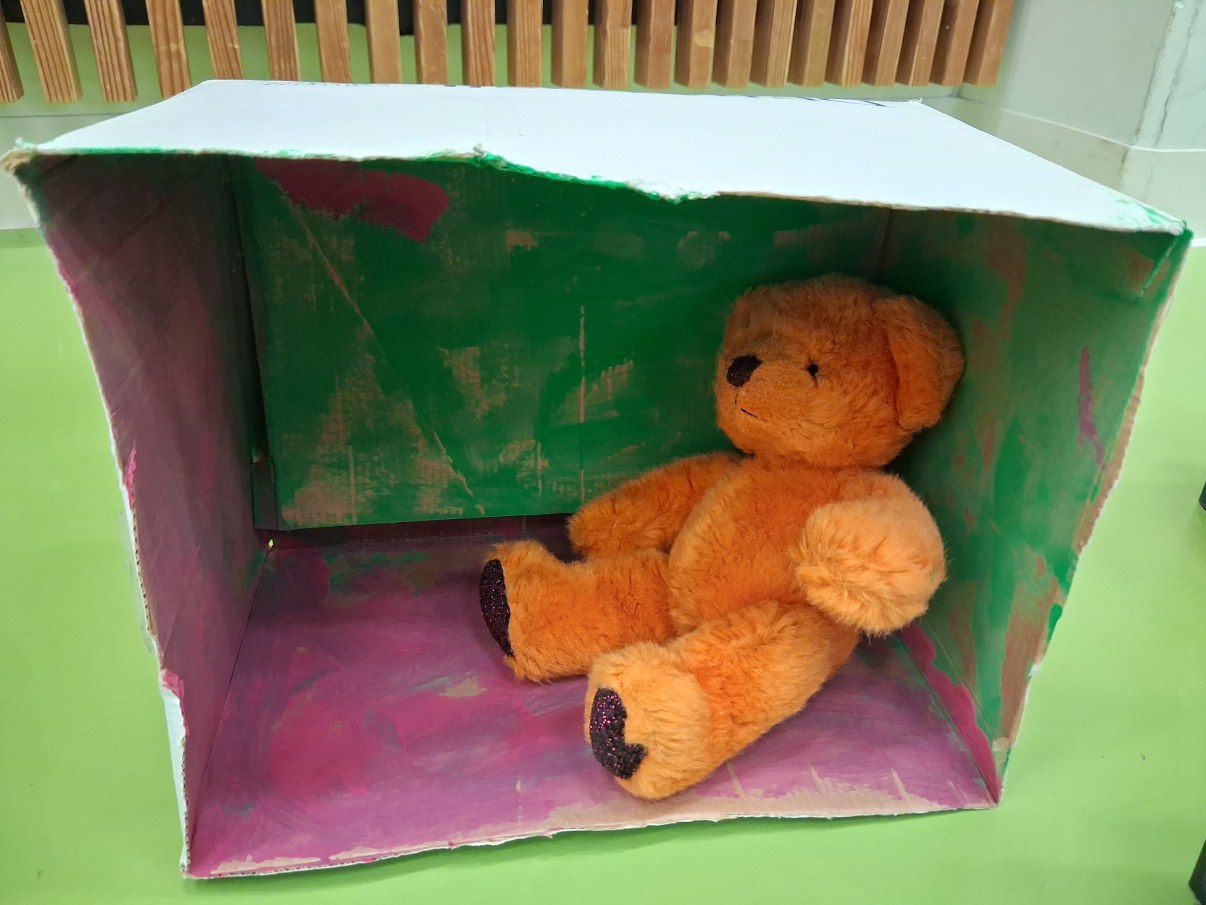 Nalle asetettuna laatikkoon, joka on askarreltu moniväriseksi.