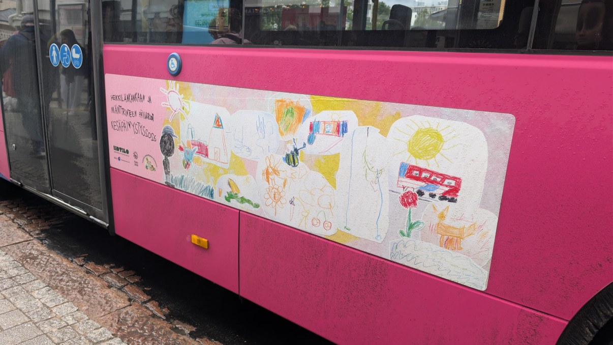 Bussin kylkeen tarroitettu suuri lasten taideteos, jossa on piirrustuksia kaupunkimaisemista. 