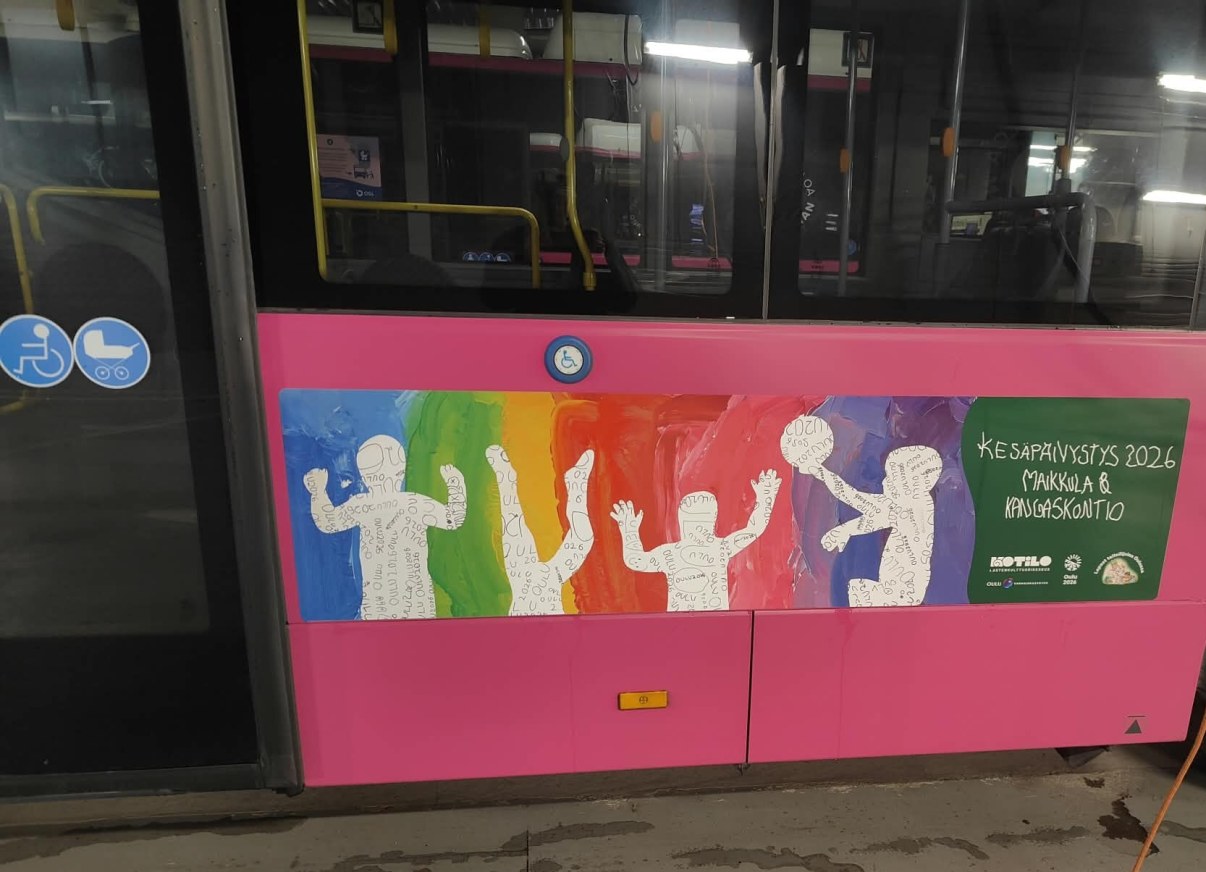 Bussin kylkeen tarroitettu suuri lasten taideteos, jossa on neljä lapsihahmoa värikkäällä taustalla sekä pallo.