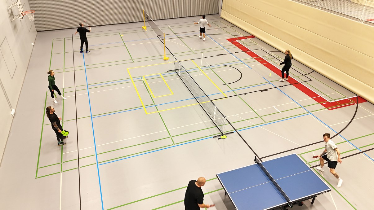 7 henkilöä pelaa mailapelejä. Sulkapallo, pickleball ja pöytätennis