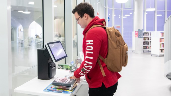 Henkilö lainaa kirjoja kirjaston lainausautomaatilla.