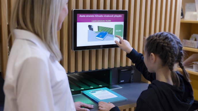 Two people are returning a book using a self-service station.